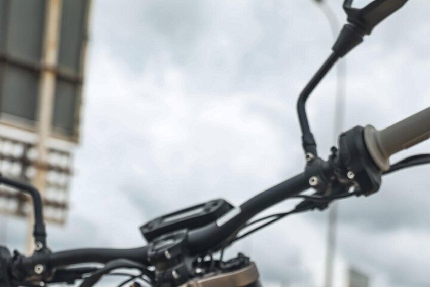 A bicycle handlebar with a control device, possibly a speedometer or GPS, and a blurred background with a building. 4