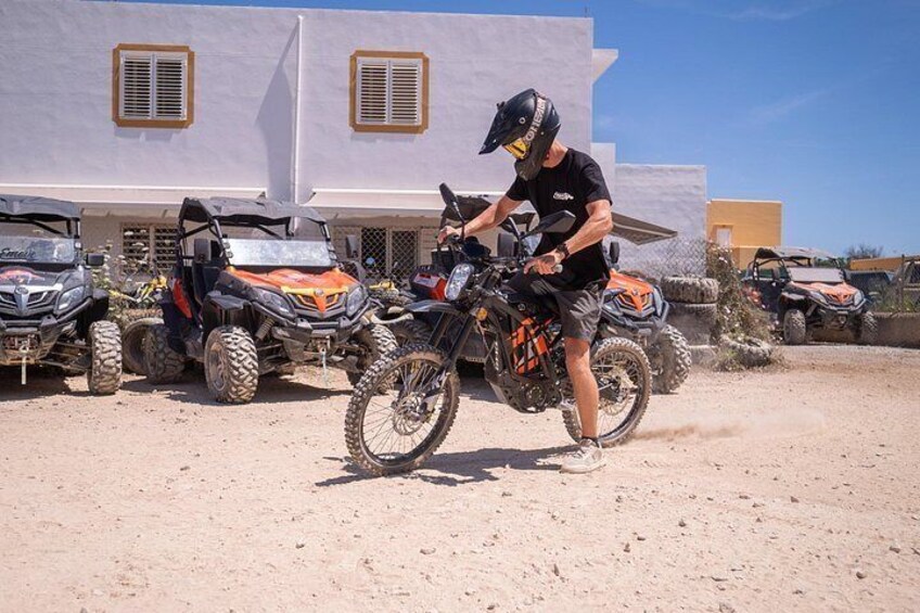Una persona conduce un cuatrimoto frente a un edificio con varias motocicletas de terreno estacionadas. 1