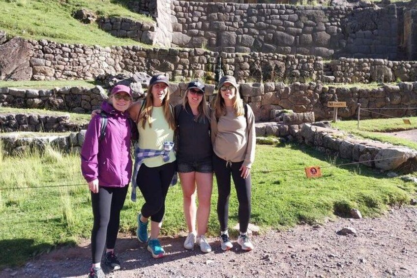 Four people standing on a dirt path with a stone wall and grassy area in the background. 2