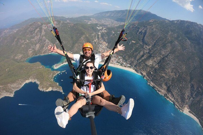 Deux personnes pratiquent le parapente au-dessus d’un paysage côtier, avec des montagnes en arrière-plan. 2