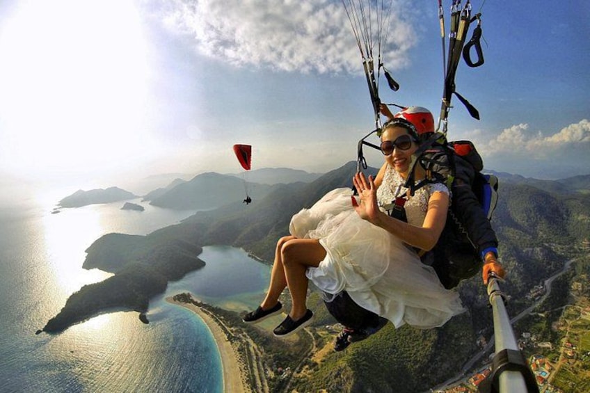 Een persoon in een witte jurk paraglidet boven een kustlandschap met bergen en een waterpartij. 1