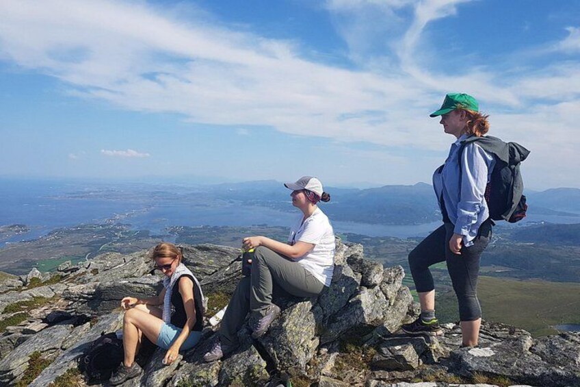 Three people sitting on a rocky outcrop with a scenic view of a valley and mountains in the background. 5