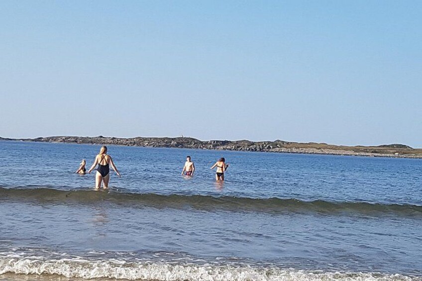 A beach with people walking in the water and a rocky shoreline in the background. 4