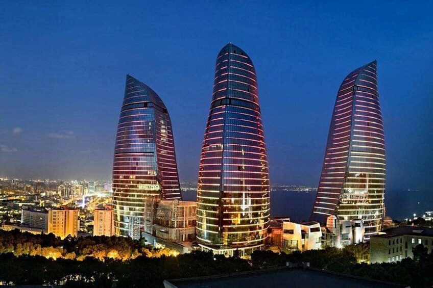 Three modern skyscrapers with unique curved designs, illuminated at night, set against a cityscape backdrop. 4