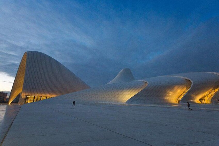 A modern architectural structure with unique curved designs, a wide open plaza, and a person walking. 2