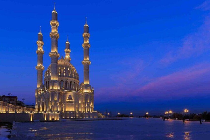A large, illuminated mosque with multiple minarets and domes, set against a twilight sky. 5