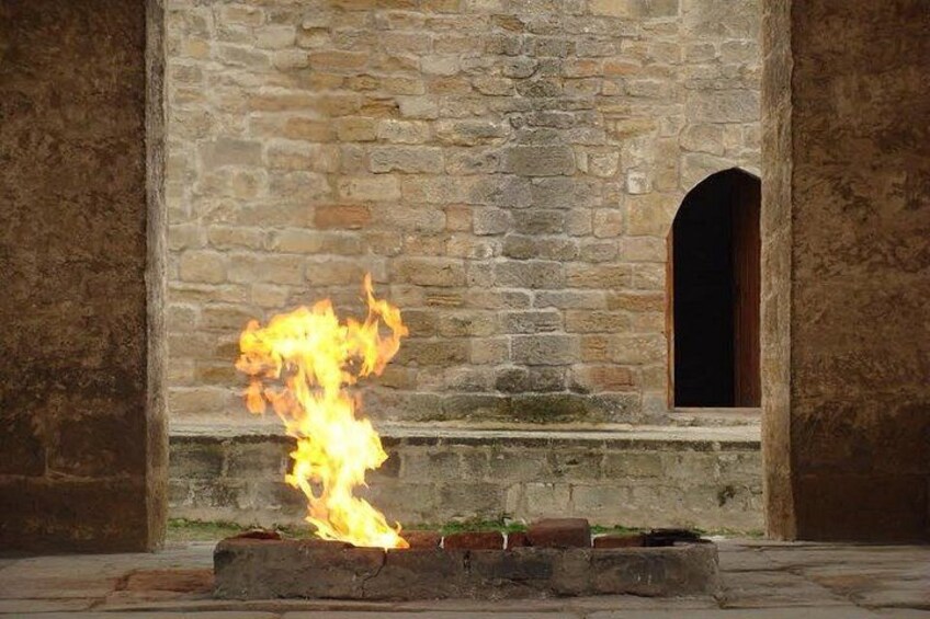 Ein Feuer brennt vor einer Steinmauer mit einem Rundbogenfenster. 3