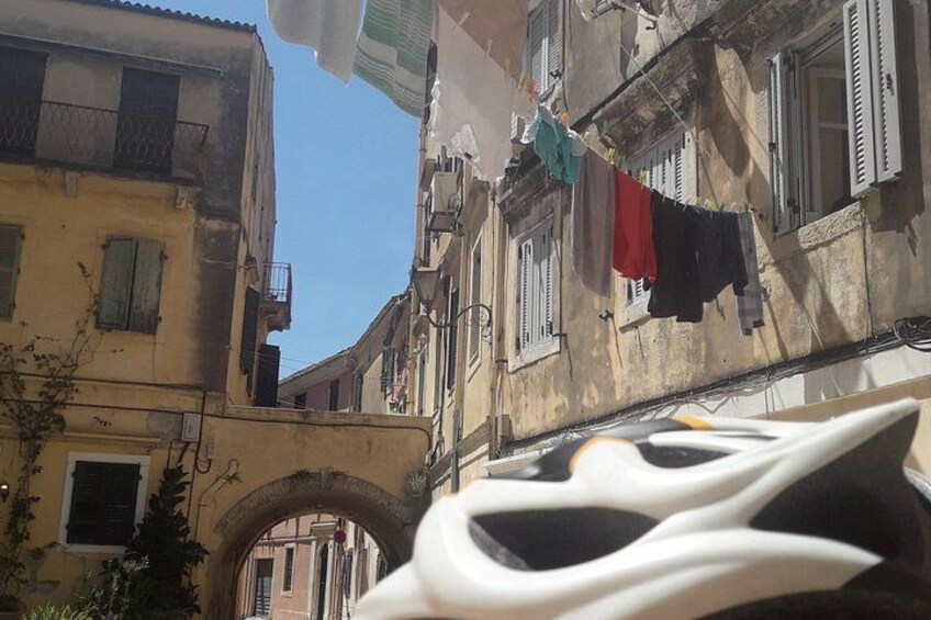 Une scène de rue avec un bateau blanc au premier plan, une arche et des bâtiments sur lesquels du linge est suspendu à des cordes. 1