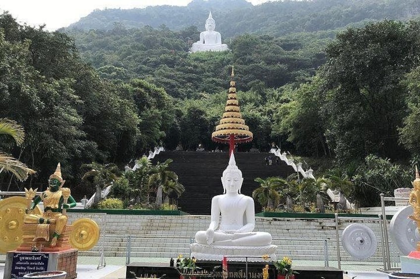 A white Buddha statue, a golden stupa, and lush greenery in the background. 1