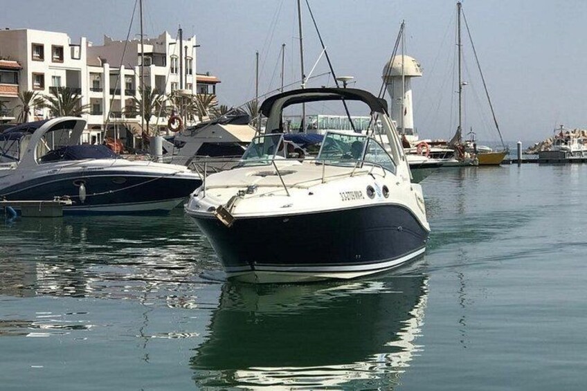 Un puerto deportivo con varias embarcaciones amarradas, un faro al fondo y un edificio de fachada blanca. 5