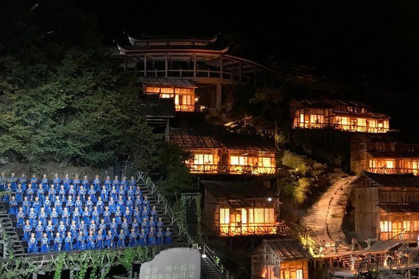 Traditional buildings with warm lighting, a group of people in blue uniforms, and a staircase leading up to the buildings. 1