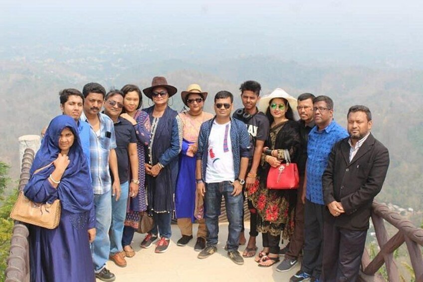 A group of people standing on a viewing platform with a mountainous landscape in the background. 1