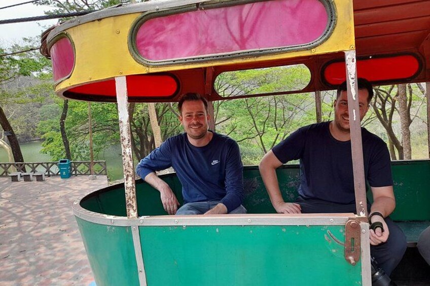 Two people seated in a green and yellow covered vehicle. 3