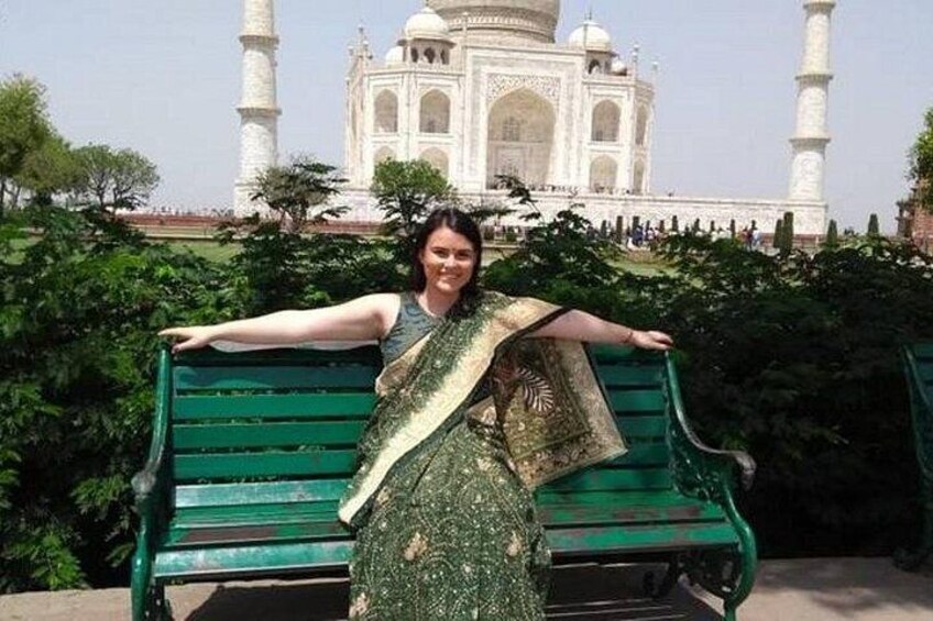 Una persona de pie frente al Taj Mahal, con un banco verde y vegetación al fondo. 4