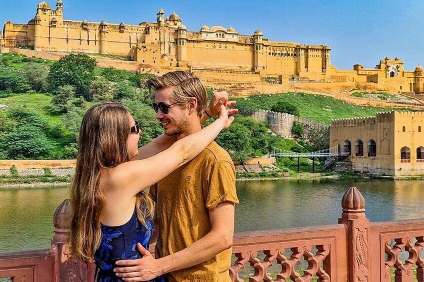 A couple embracing by a river with a historic fort in the background. 1