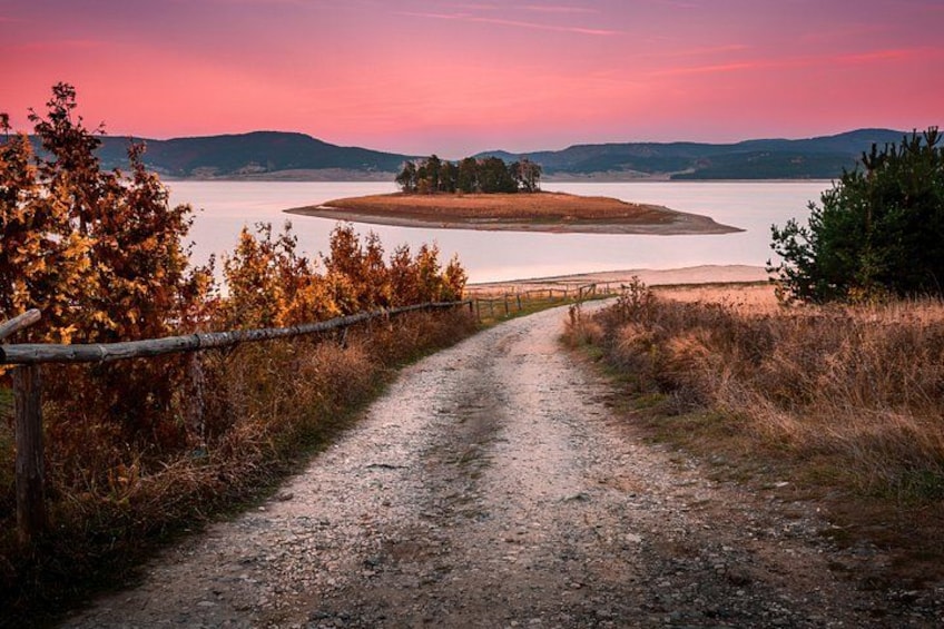 Ein Kiesweg führt zu einem See, der von Bäumen und Hügeln umgeben ist. 5