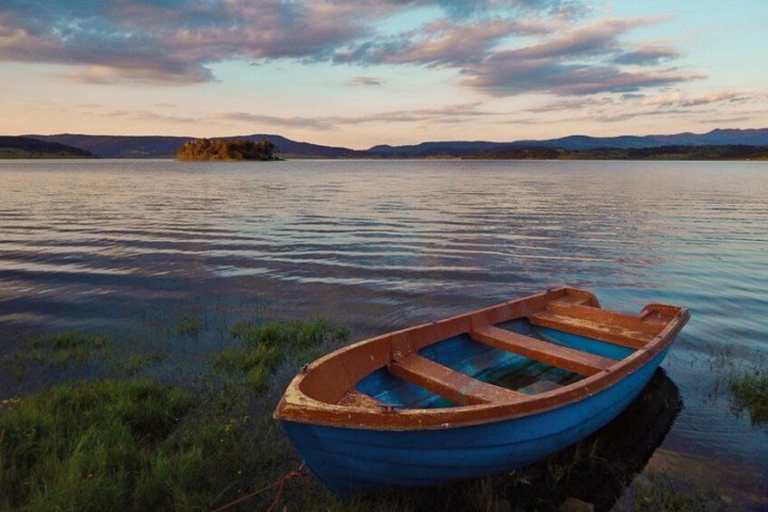 Ein kleines Holzboot auf ruhigem Wasser, im Hintergrund eine ferne Insel und Berge. 1