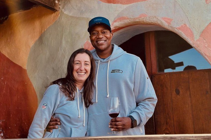 Two people standing in front of a building with a wooden door and a colorful wall. 3