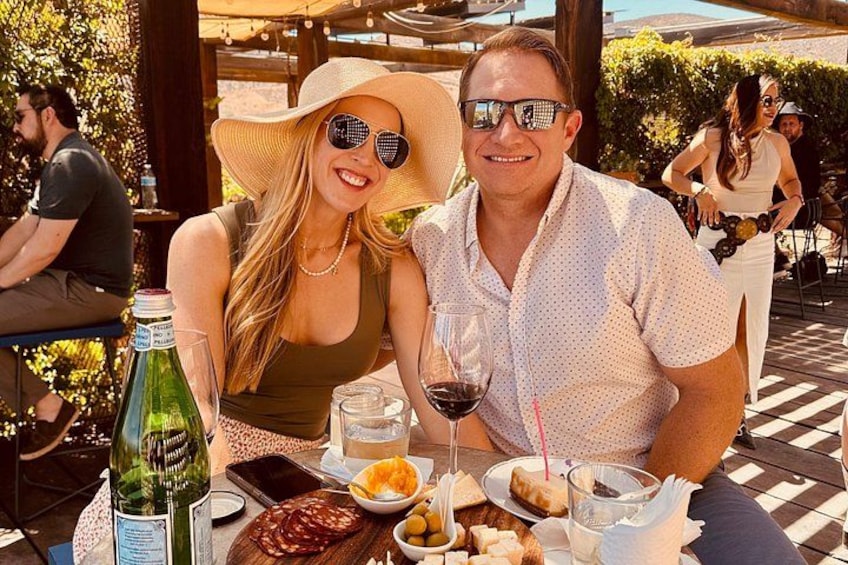 Two people sitting at an outdoor table with food and drinks. 1