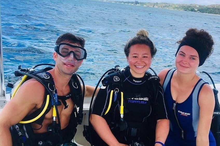 Three people wearing scuba diving gear on a boat with the ocean in the background. 4