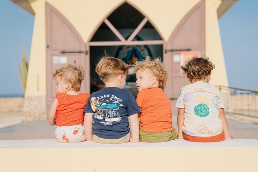 Cuatro niños sentados en un alféizar frente a un edificio con puertas de arco. 4