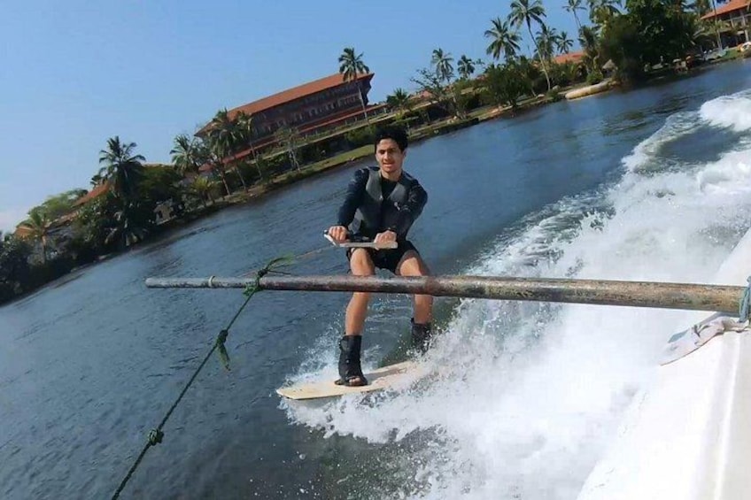 Iemand wakeboard op een rivier, met palmbomen en gebouwen op de achtergrond. 1