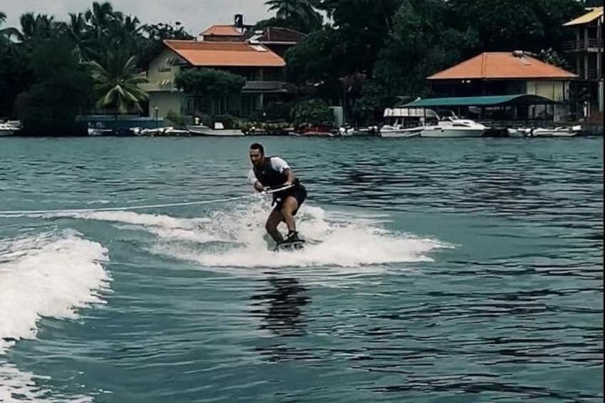 Iemand wakeboard op een wateroppervlak, met huizen en boten op de achtergrond. 2