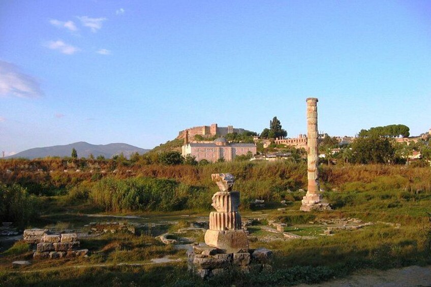 Ancient ruins with columns and stone statues, a hilltop fortress, and a clear sky. 2