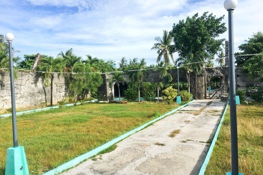 A pathway with a concrete surface, bordered by green-painted edges, leading to a structure with a stone wall and vegetation. 4