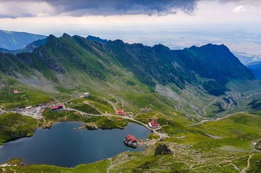 A mountainous landscape with a lake, a small settlement with buildings, and a winding road. 1