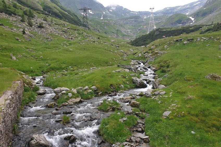 A mountain stream flowing through a valley with rocky terrain and green grass. 4