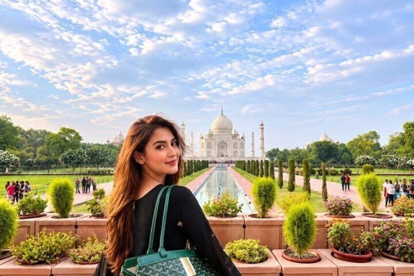 A person standing in front of the Taj Mahal with a garden and a clear sky in the background. 3