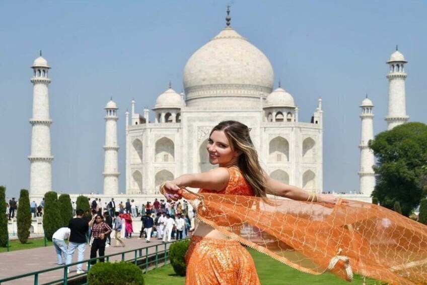 A person in an orange outfit with a patterned shawl in front of the Taj Mahal. 1