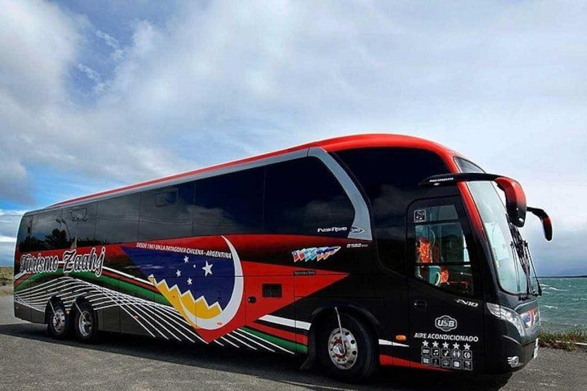 A red and black bus with a colorful design, parked by the sea. 3