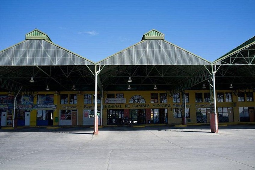 A train station with a green roof, yellow walls, and multiple signs including 'Welcome' and 'Terminal de Omibus Municipal.' 5