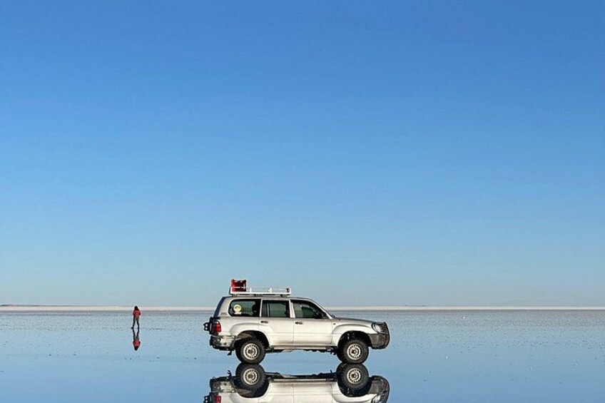 Un SUV blanco estacionado sobre una superficie acuática reflectante con un cielo despejado al fondo. 2
