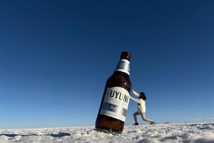 Una botella de cerveza UYUNI sobre nieve, con una persona al fondo. 3