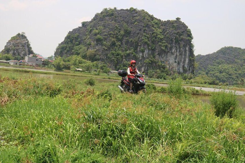A person riding a motorcycle through a grassy area with a large rock formation in the background. 2