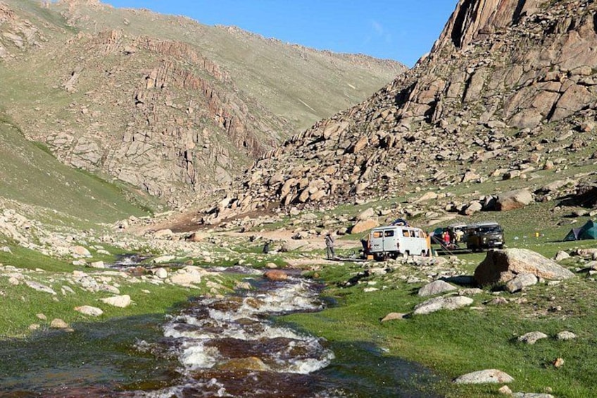 A mountainous landscape with a stream, rocky terrain, and a white van parked near the stream. 5