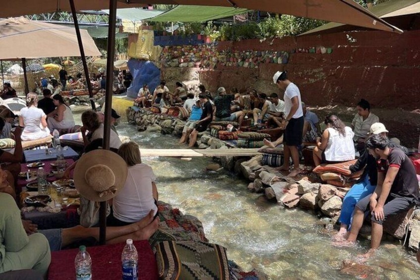 Un grupo de personas reunidas alrededor de una fuente de agua, con un muro de piedra y una estructura de madera. 5