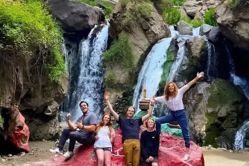 A group of people posing in front of a waterfall with a rocky backdrop. 1