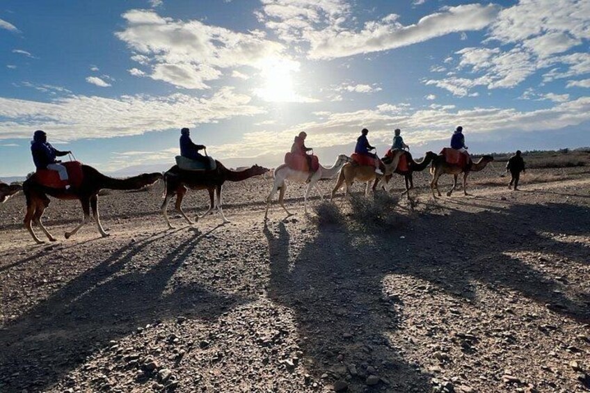 En gruppe mennesker rider på kameler over et stykke stenet terræn under en klar himmel. 2