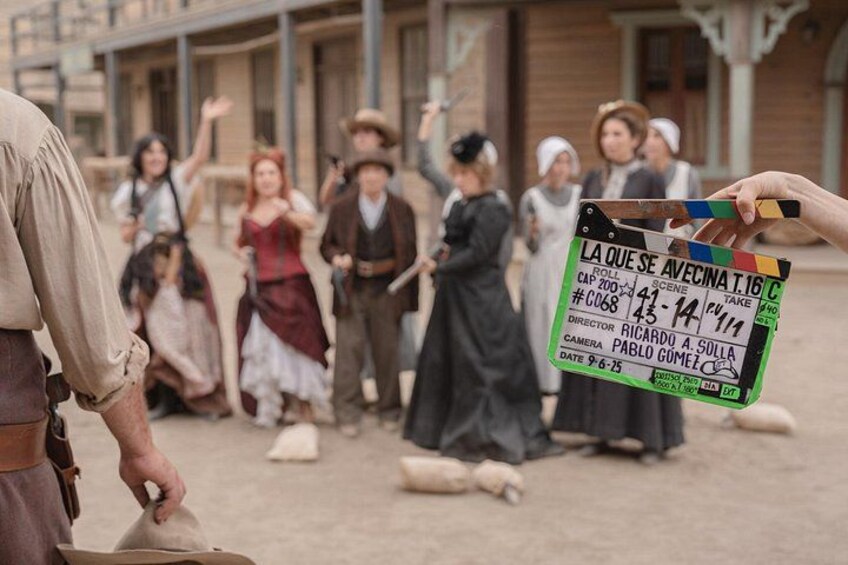 A film set with a clapperboard, actors in period costumes, and a building in the background. 3