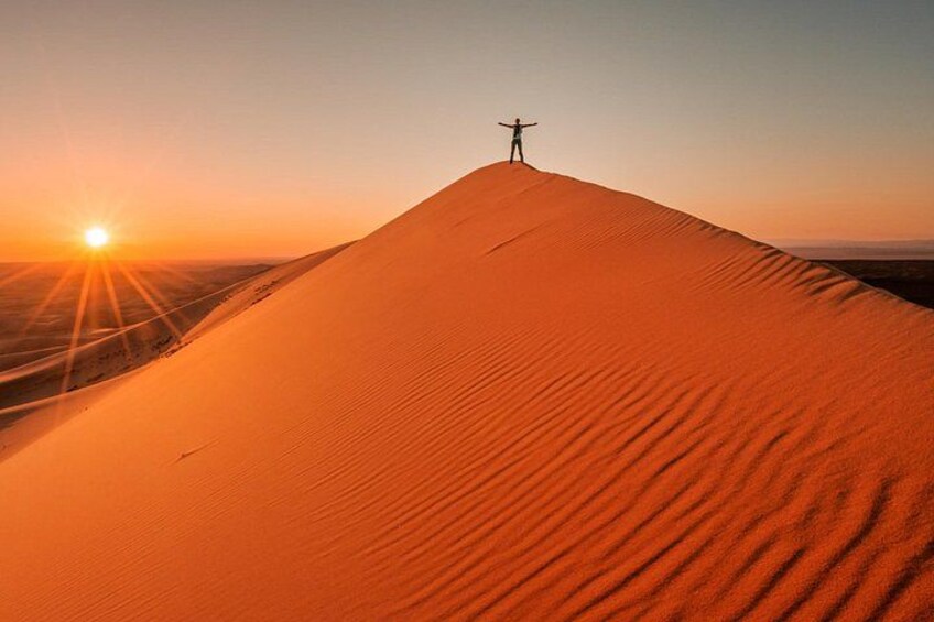 A desert landscape with a person standing on a sand dune at sunset. 3