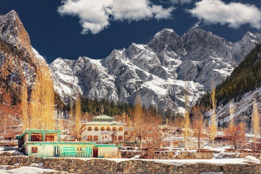 A mountainous landscape with snow-covered peaks, a traditional building with a green roof, and leafless trees in the foreground. 1