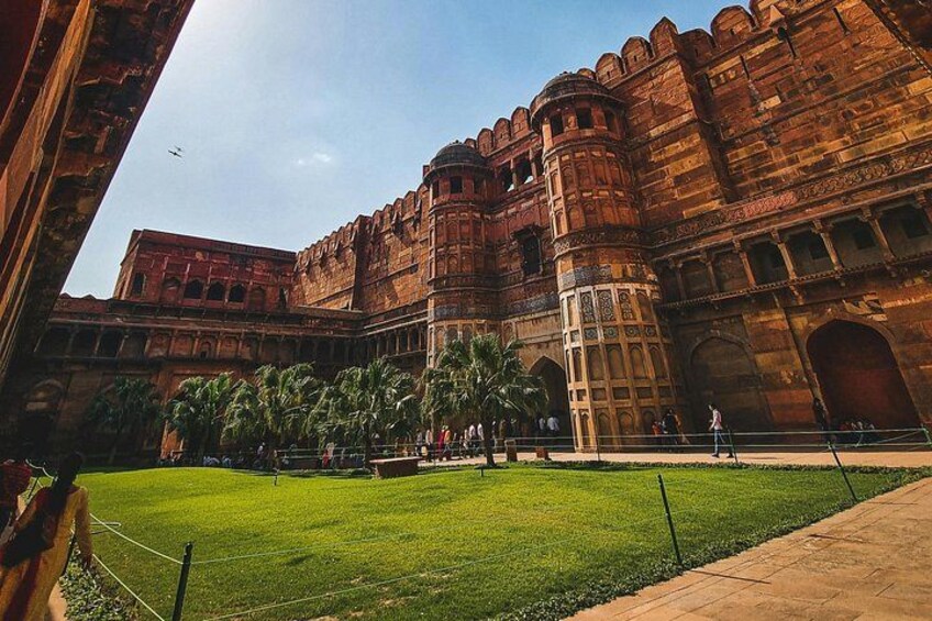 A large, historic building with intricate architecture, a well-maintained lawn, and a clear sky. 3