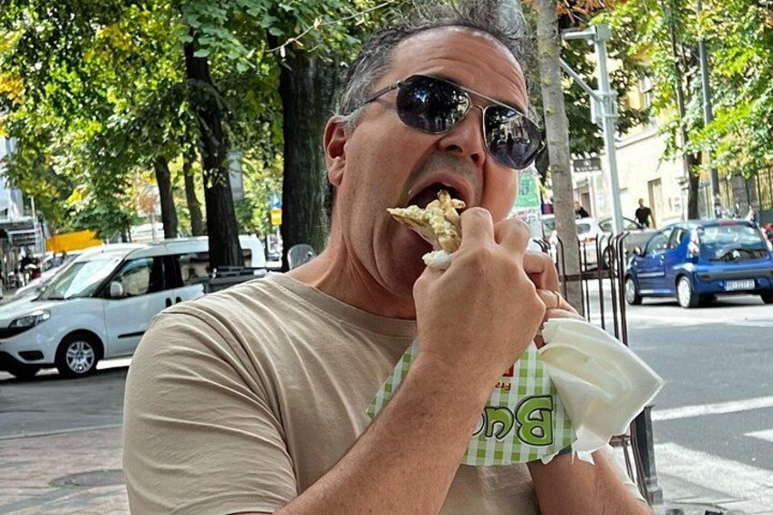 A person eating food outdoors with trees and parked cars in the background. 2