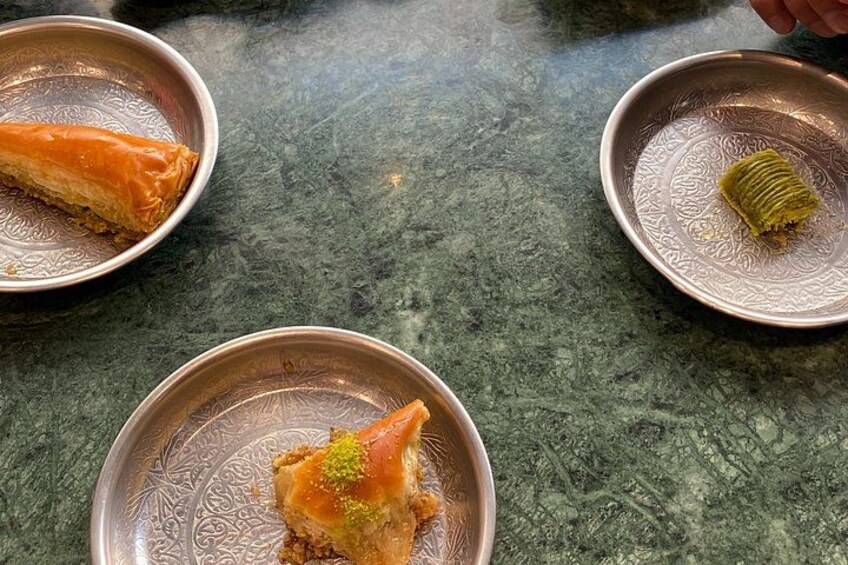 Three metal plates with pieces of baklava on a textured surface. 5