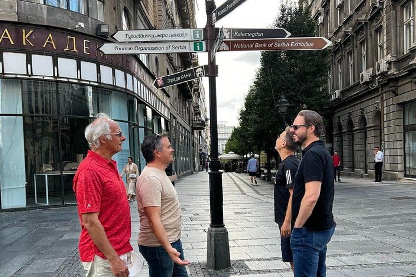 A group of people standing on a city street with a signpost indicating directions to various landmarks. 4