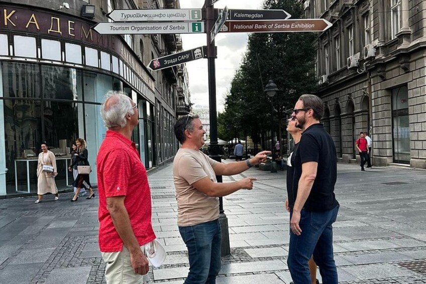 Three people on a city street with signs for tourism and banking. 3